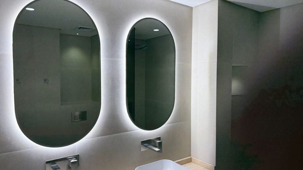 Seamless microcement bathroom walls in a Dubai villa with backlit oval mirrors and wall-mounted taps
